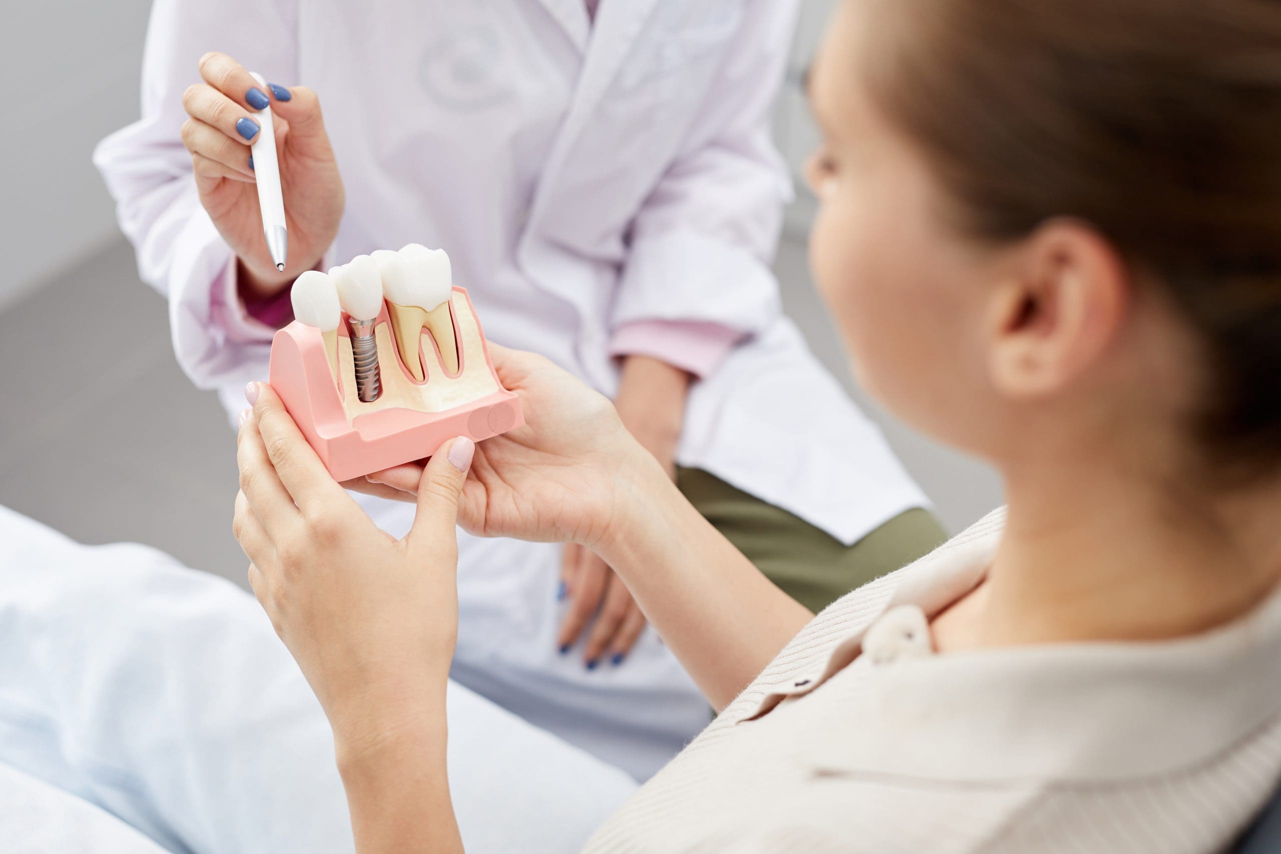 Closeup of female doctor pointing at dental implant model to a female patient